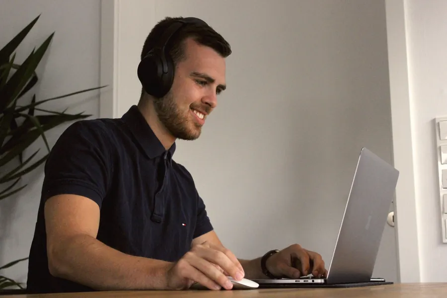 A salesperson smiling on a call with a headset at his laptop