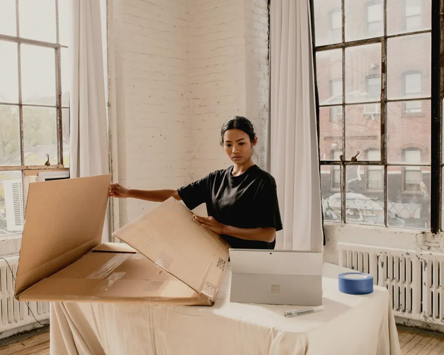 A store owner folding a shipping box beside her laptop in a bright studio