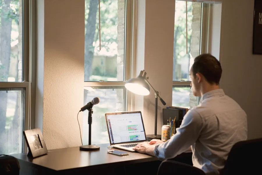 A salesperson on a call at his desk by the window, microphone and laptop in front of him
